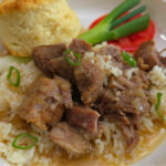 Country-Style Stewed Pork Meat and Rice Recipe with broth served in a white bowl with a buttermilk biscuit, green onion, and rip tomato slice